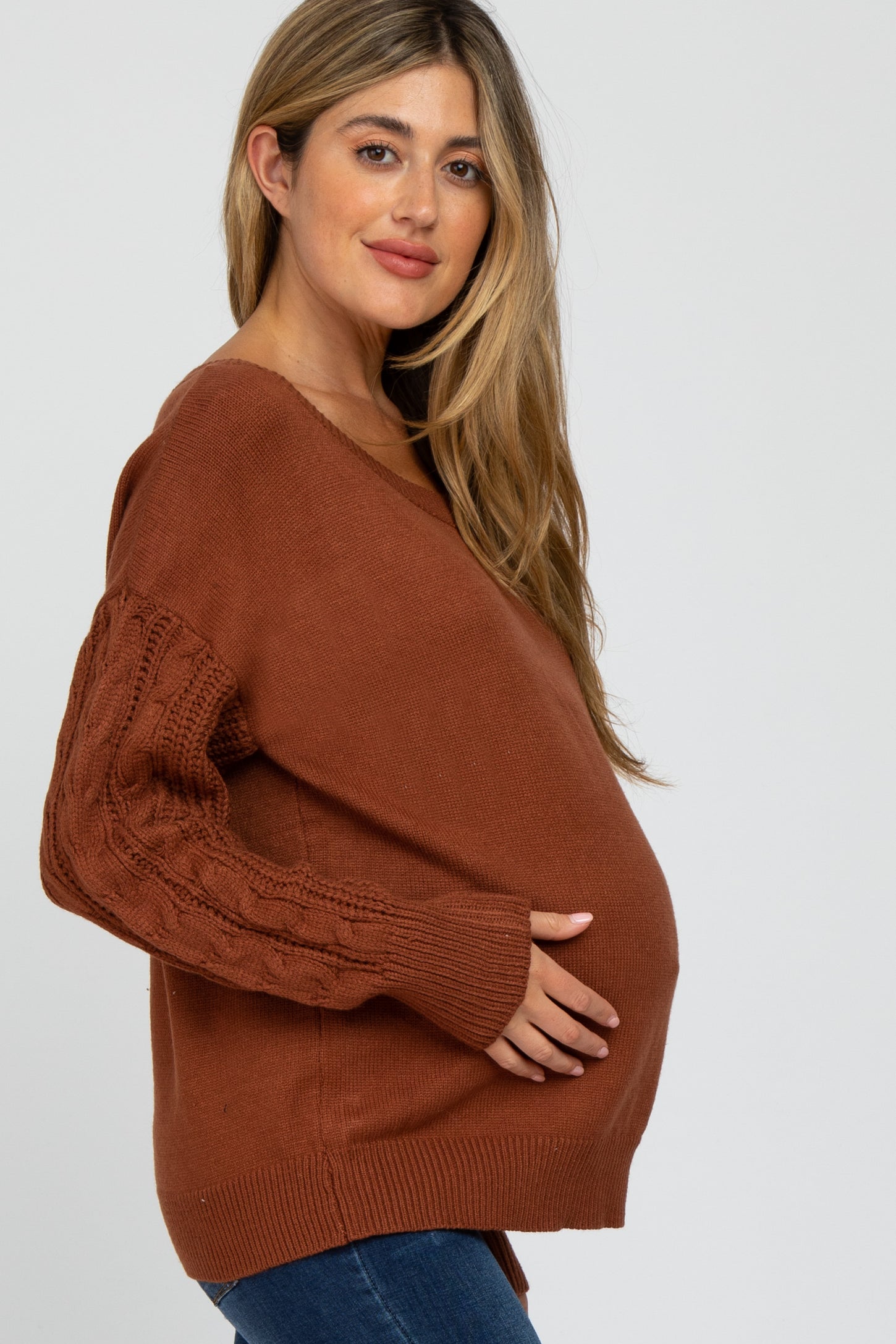 woman wearing a rust-colored maternity sweater with cable knit sleeves and holding her baby bump