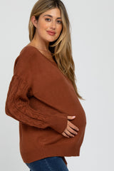 woman wearing a rust-colored maternity sweater with cable knit sleeves and holding her baby bump