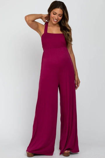 woman wearing a fuchsia maternity jumpsuit with a smocked bodice and wide leg style, showing her baby bump