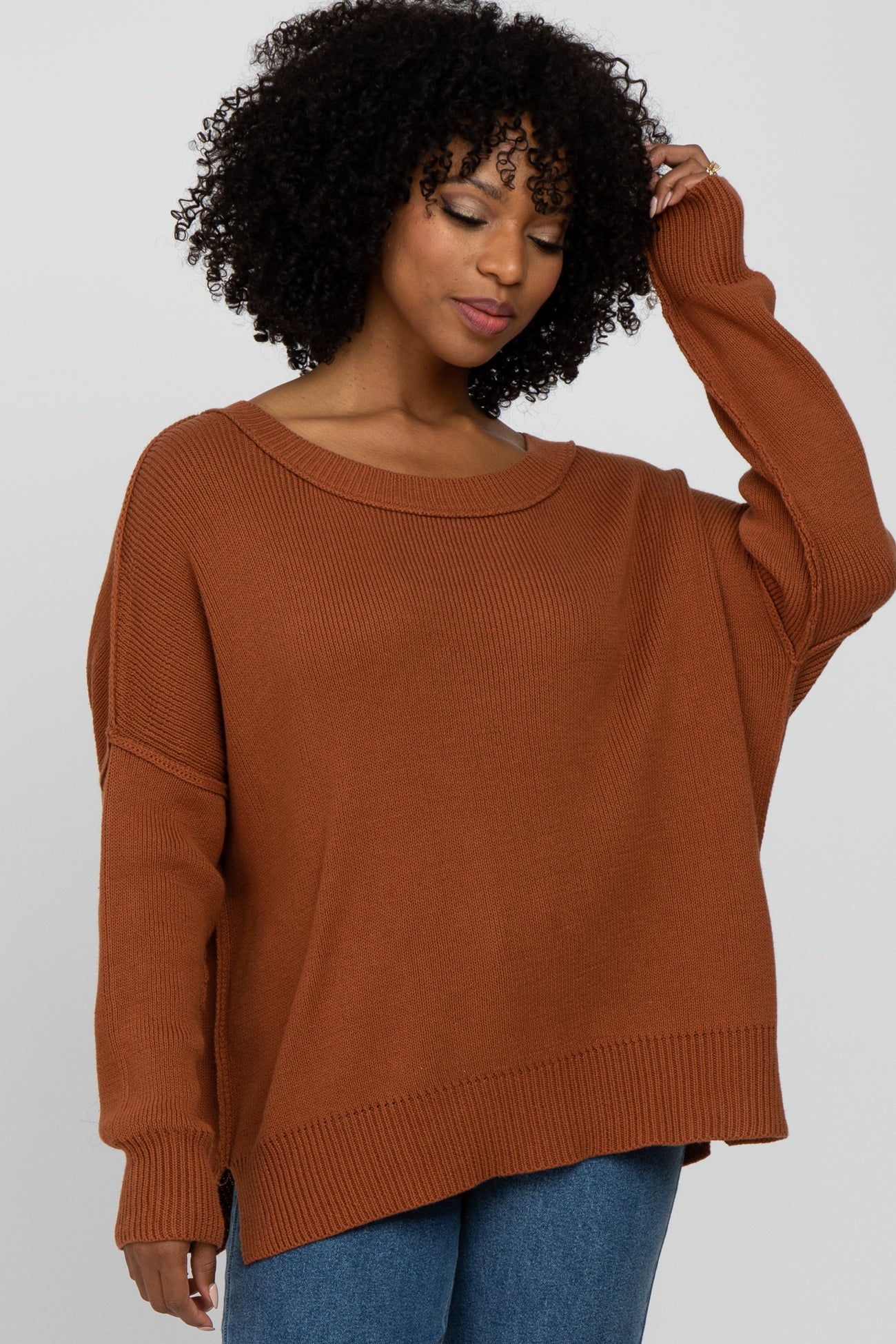 woman wearing a rust oversized sweater with a wide neckline and ribbed cuffs, paired with denim jeans