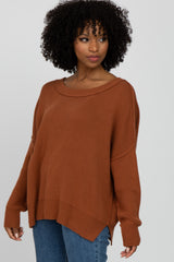 woman wearing a rust oversized sweater with a wide neckline and side slits, paired with blue jeans