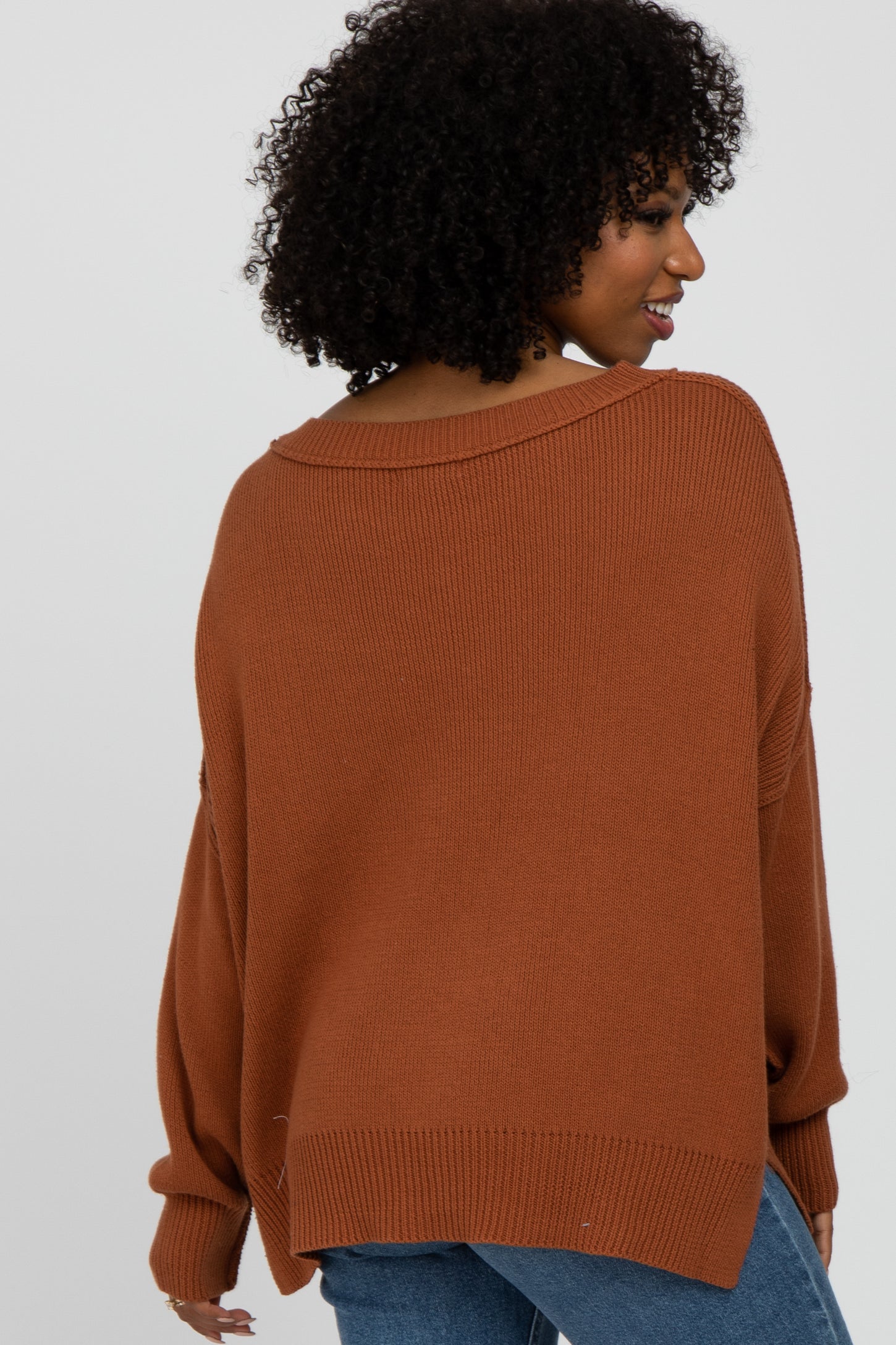 woman wearing a rust oversized sweater with a wide neckline and ribbed texture, shown from the back