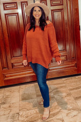 woman wearing an orange oversized sweater and blue skinny jeans, accessorized with a beige hat and nude heels