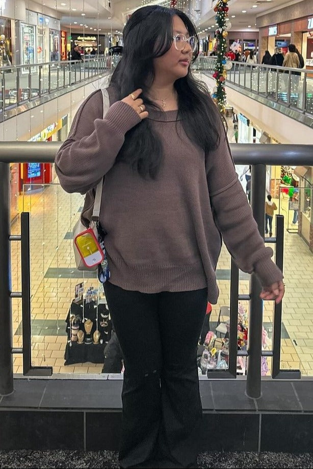 woman wearing a brown oversized sweater and black flared pants standing in a shopping mall