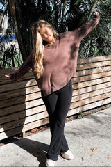 woman wearing a brown oversized sweater and black flared pants, standing outdoors with a relaxed pose