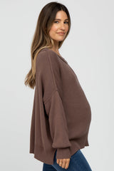 woman wearing a brown oversized maternity sweater and showing her baby bump