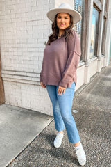 woman wearing a mauve oversized sweater, light blue jeans, and white sneakers, standing outside with a wide-brim hat