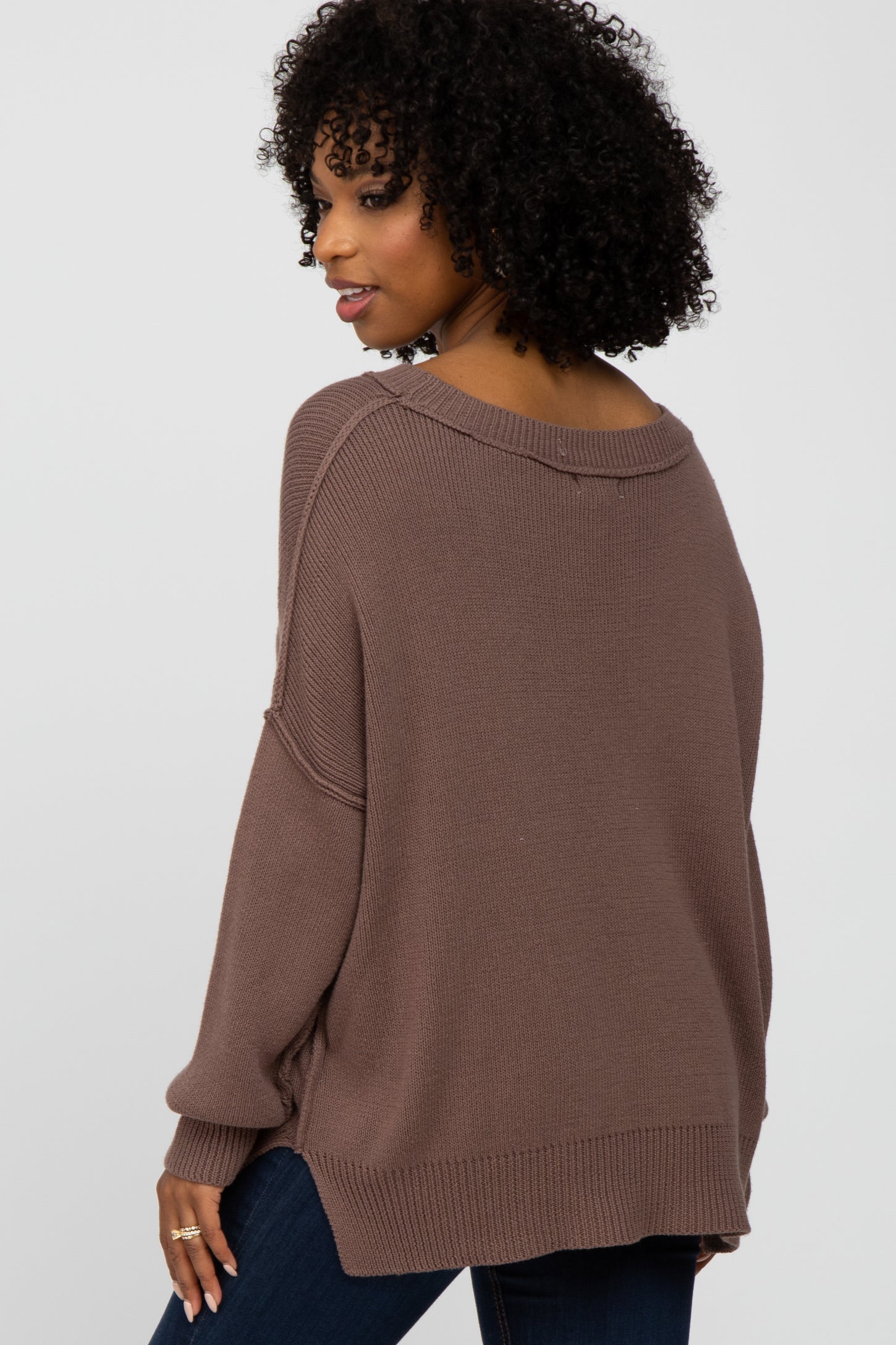 woman wearing a taupe oversized sweater with a scoop neck and side slits, shown from the back