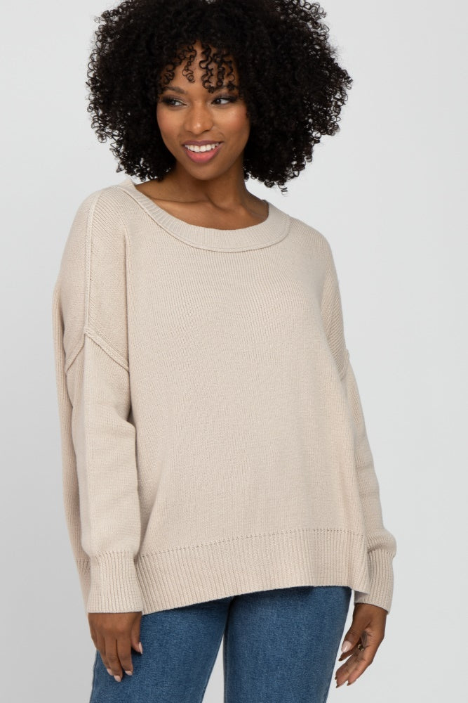 woman wearing a beige oversized sweater with a wide neckline and relaxed fit, paired with blue jeans