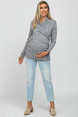 woman wearing a gray wrap maternity top and light blue jeans, holding her baby bump