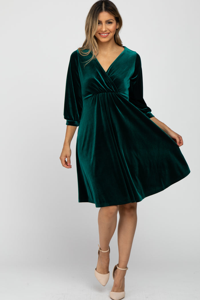 woman wearing a dark green velvet wrap dress with three-quarter sleeves and a flared skirt