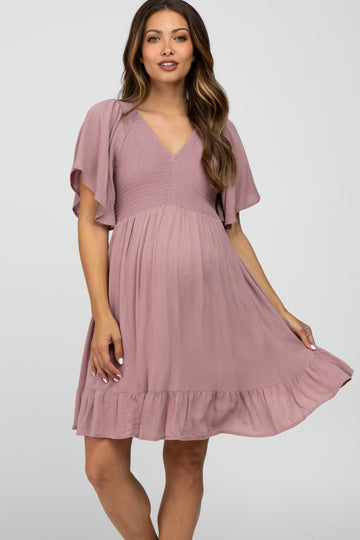 woman wearing a mauve maternity dress with flutter sleeves, a smocked bodice, and a ruffled hem, highlighting her baby bump