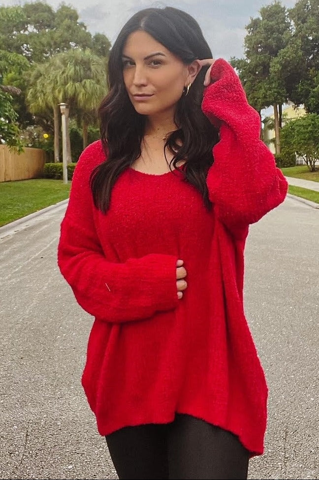 woman wearing a bright red oversized sweater and black leggings, posing outdoors in a scenic setting