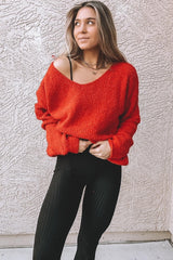 woman wearing a loose red oversized sweater and black ribbed leggings, standing against a textured wall