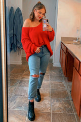 woman wearing a red oversized knit sweater and distressed light blue jeans, posing in front of a mirror