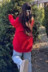 woman wearing a slouchy red sweater and light blue jeans standing next to a tree