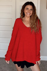 woman wearing a bright red oversized sweater with a v-neckline and black shorts, smiling at the camera