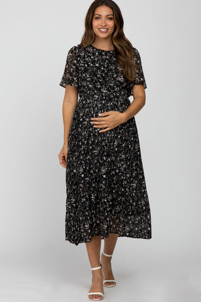 woman wearing a black floral print maternity dress with short sleeves and a flowing skirt, holding her baby bump