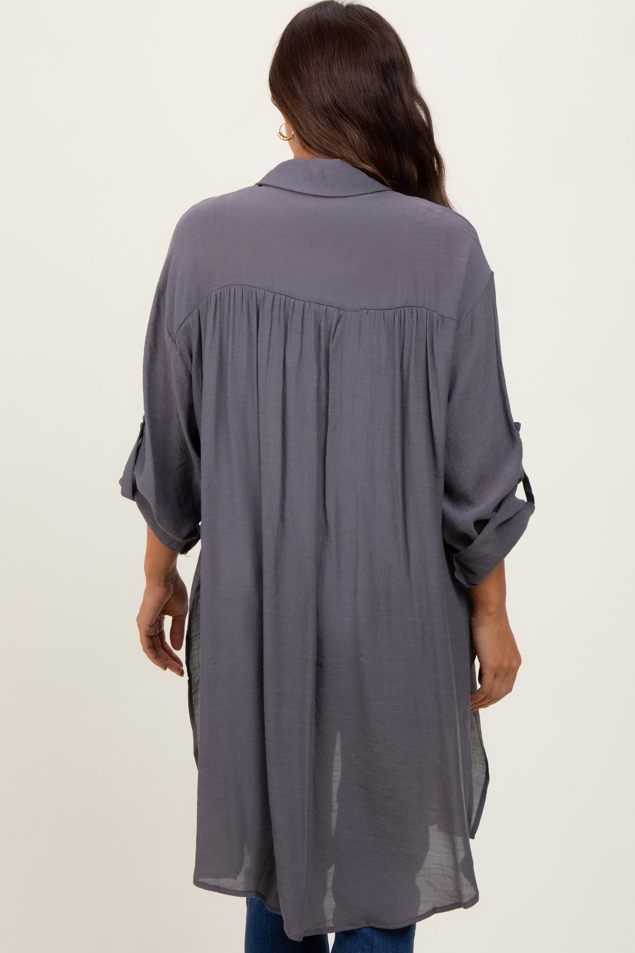 Back view of a woman wearing a long charcoal grey button down tunic shirt with pleated back detail