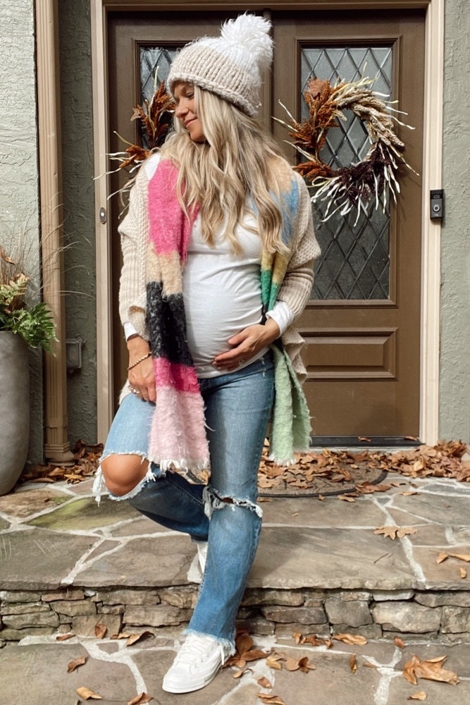 woman wearing a white tank top, cream cardigan, distressed jeans, and a colorful scarf, showing her baby bump outdoors