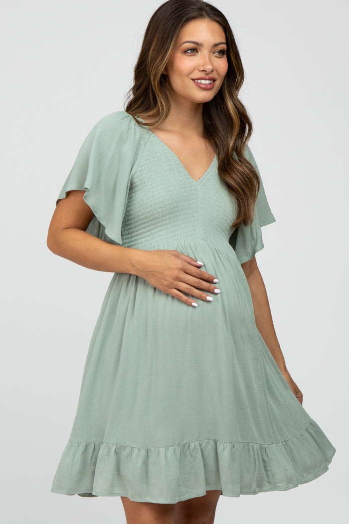 woman wearing a mint green maternity dress with flutter sleeves and a ruffled hem, holding her baby bump