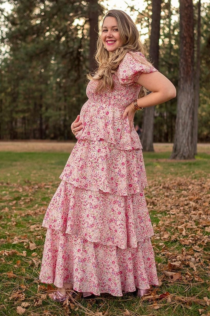 woman wearing a pink floral maternity maxi dress with tiered ruffles and a visible baby bump