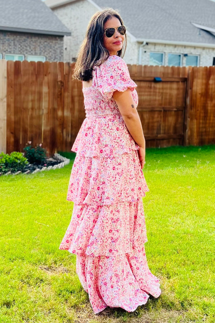 woman wearing a pink floral maxi dress with tiered ruffle details, standing in a garden with sunglasses on