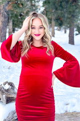 woman wearing a red velvet maternity dress with bell sleeves and a visible baby bump in a snowy outdoor setting