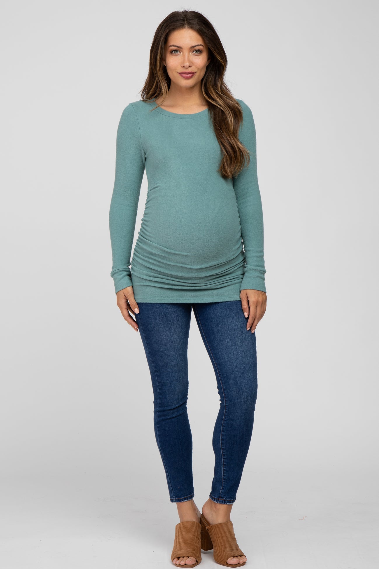 woman wearing a teal long sleeve maternity top with side ruching and blue skinny jeans, showing her baby bump