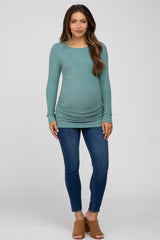 woman wearing a teal long sleeve maternity top with side ruching and blue skinny jeans, showing her baby bump