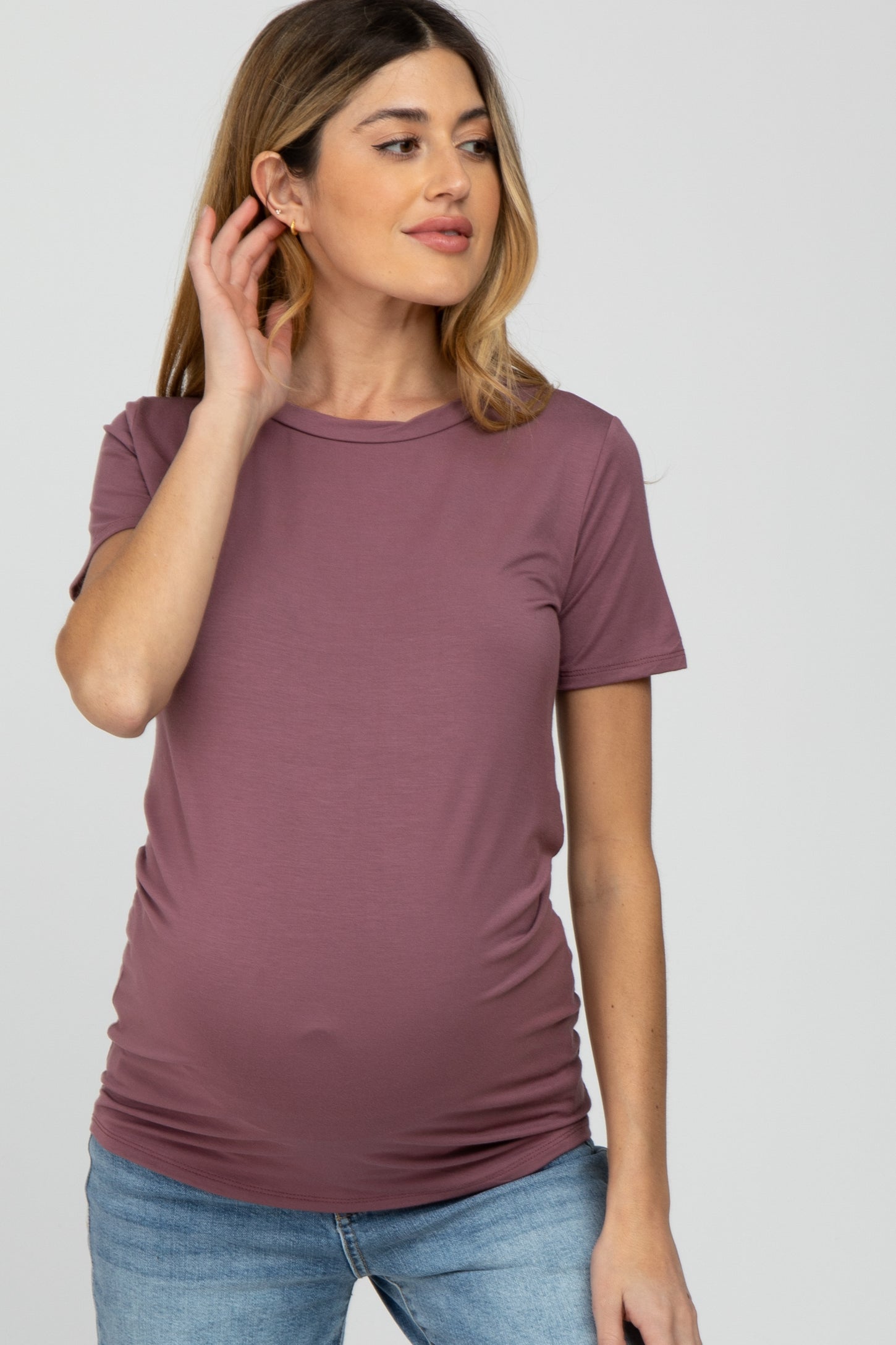woman wearing a mauve short sleeve maternity top and highlighting her baby bump