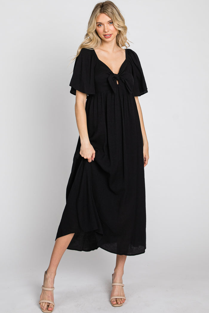 woman wearing a black maxi dress with a v-neckline, short flutter sleeves, and a knotted detail at the bust