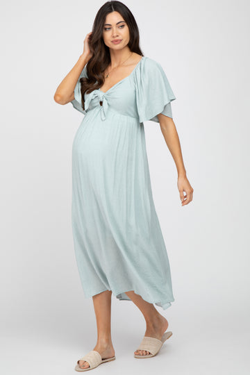 woman wearing a light blue maternity dress with flutter sleeves and a tie front, showcasing her baby bump