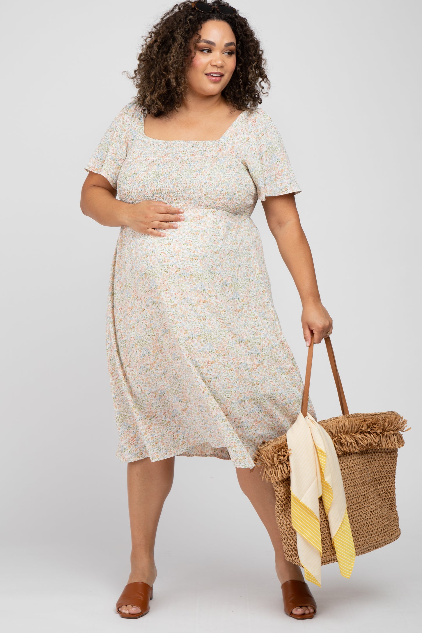 woman wearing a floral print maternity dress with a square neckline and short sleeves, holding a bag and showing her baby bump
