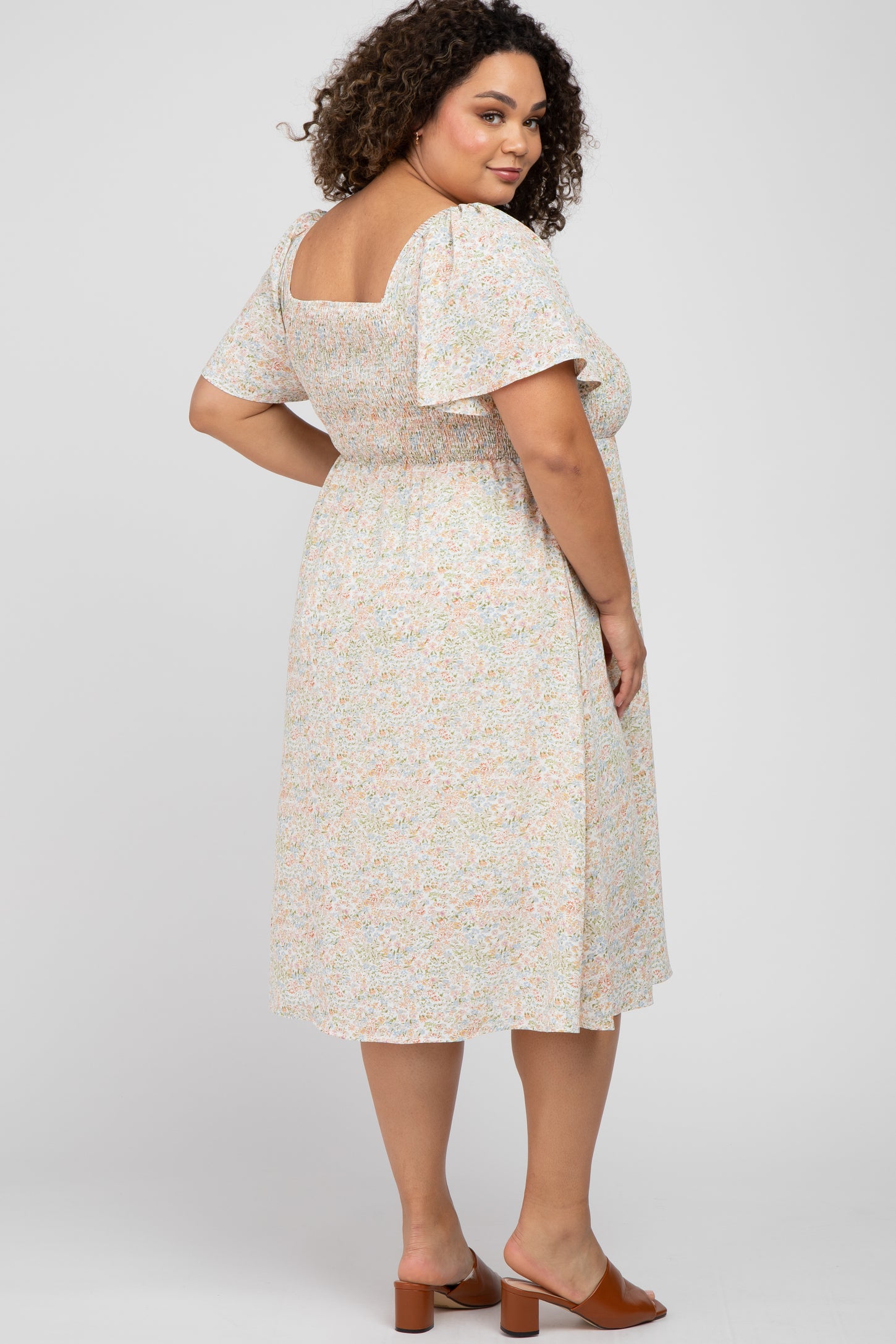 woman wearing a floral print maternity plus dress with a square neckline and flutter sleeves, showing her baby bump from the back