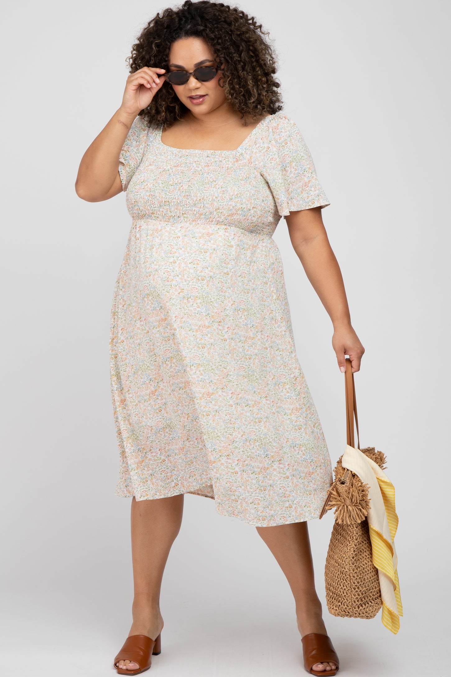 woman wearing a floral maternity plus dress with short sleeves and a square neckline, holding a bag and wearing sunglasses