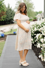 woman wearing a light floral maternity dress and holding her baby bump while standing outdoors