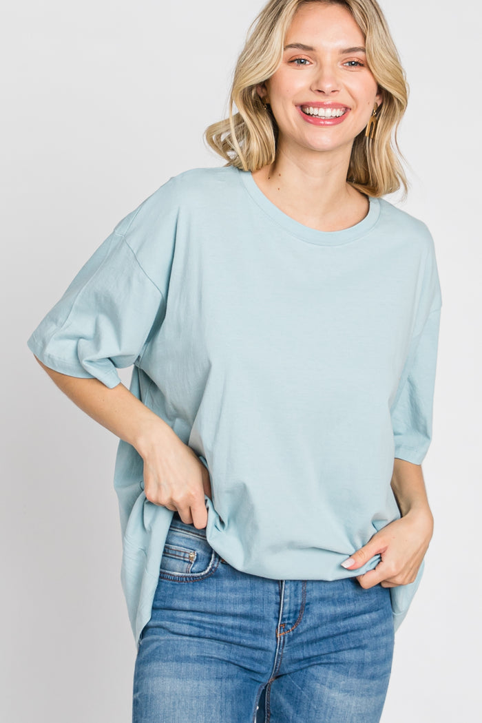 woman wearing a light blue oversized t-shirt and jeans, smiling at the camera