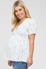 Pregnant woman wearing a white and blue floral maternity wrap top with short puff sleeves