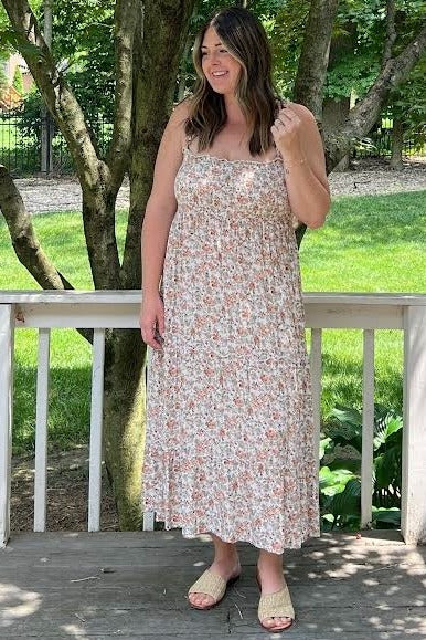 woman wearing a floral maxi dress with spaghetti straps and a tiered skirt, standing outdoors on a porch