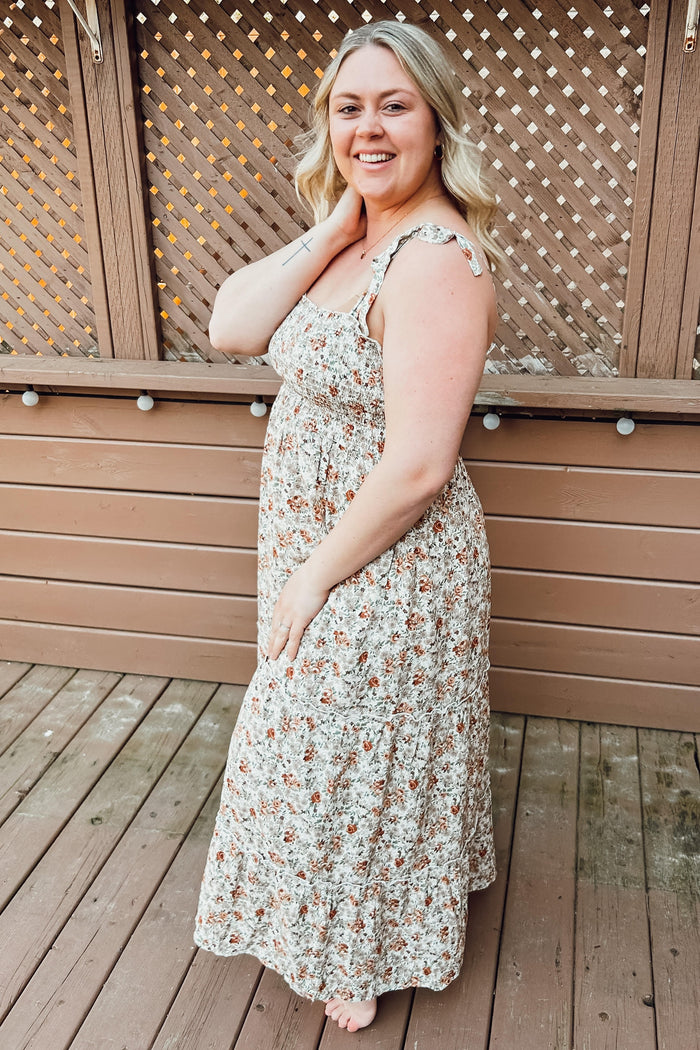 woman wearing a floral print maxi dress with adjustable straps and a smocked bodice, standing on a wooden deck
