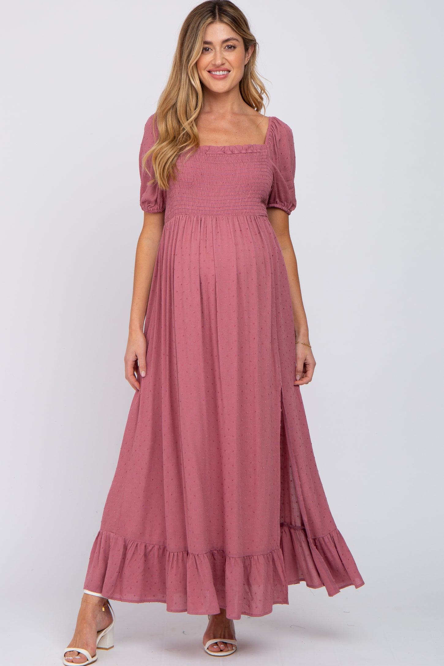 woman wearing a rose pink maternity maxi dress with puff sleeves and a tiered ruffle hem, showing off her baby bump
