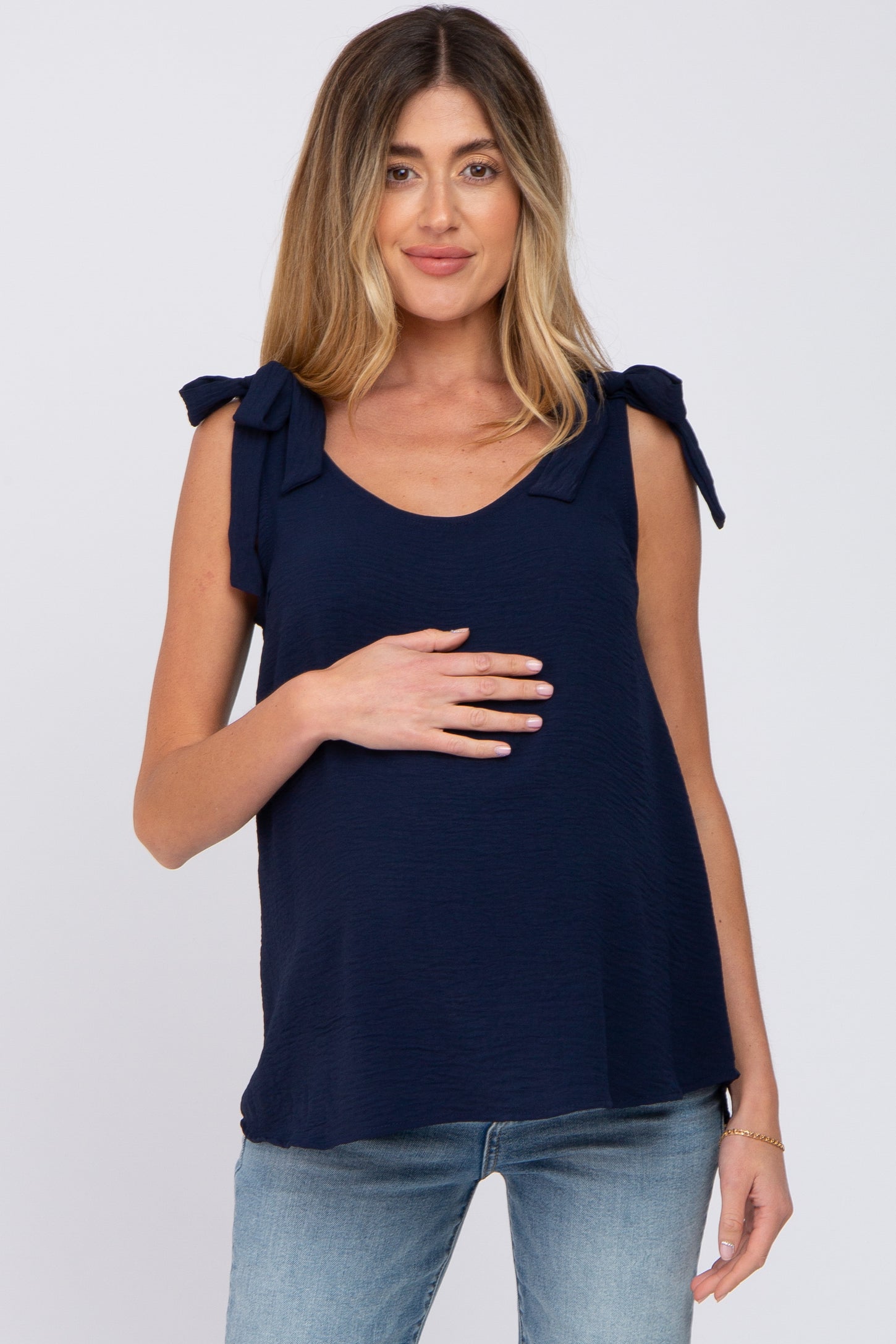 woman wearing a navy blue maternity top with tie shoulder details and holding her baby bump