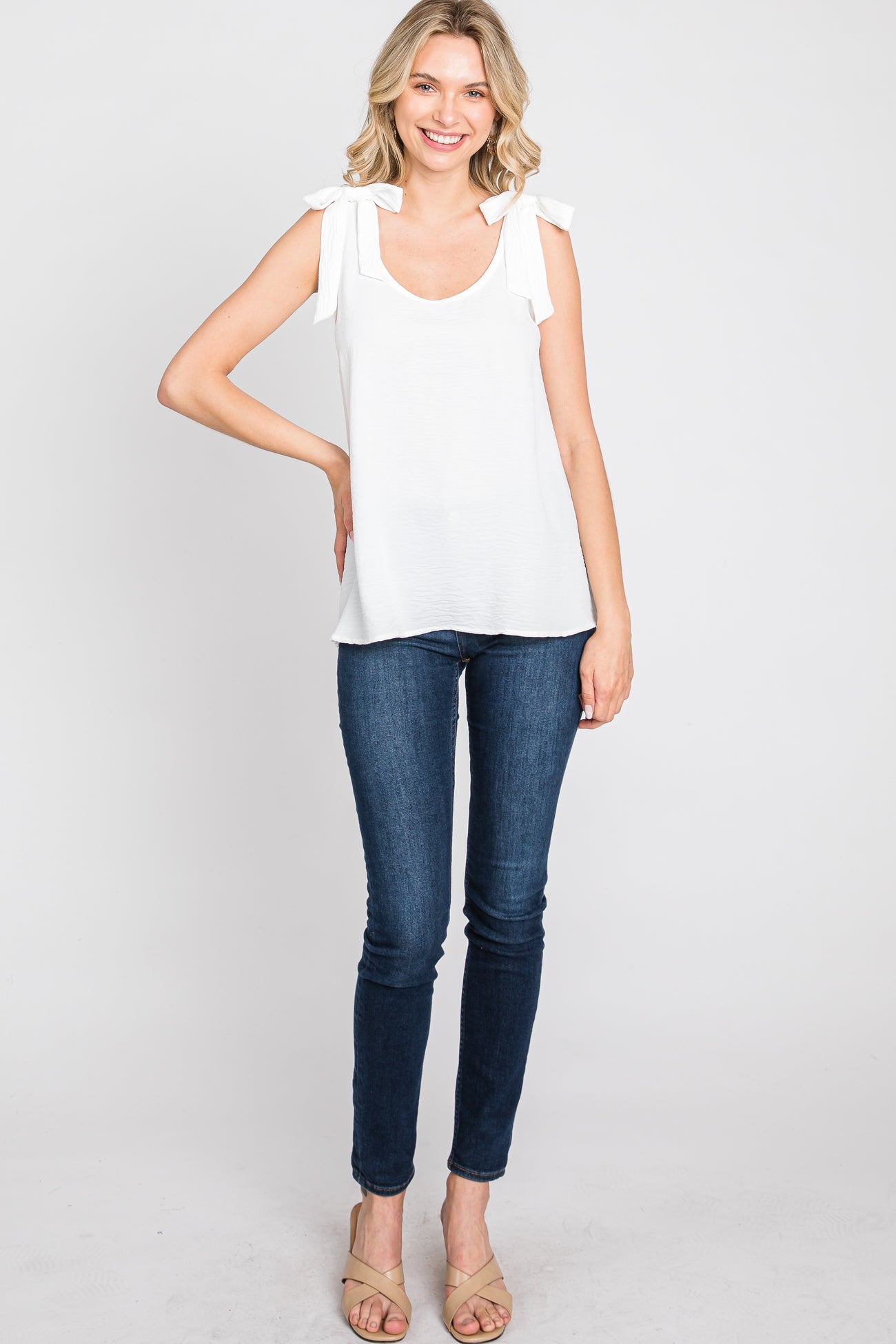 woman wearing a white sleeveless top with bow details and blue skinny jeans