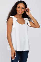 woman wearing a white sleeveless top with tie shoulder details and a relaxed fit, paired with denim jeans