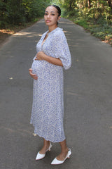 woman wearing a blue floral print maternity dress and holding her baby bump on a path in the woods