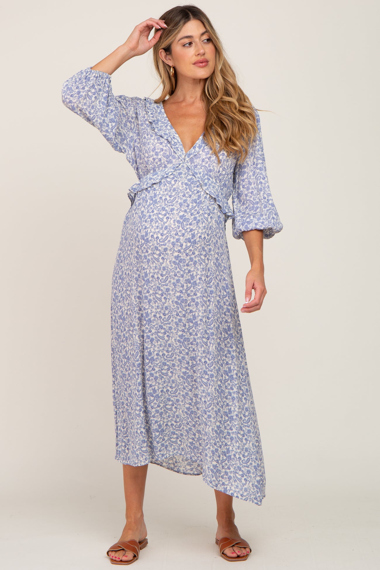 woman wearing a blue floral print maternity wrap dress, displaying her baby bump, with long sleeves and an asymmetrical hem
