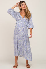 woman wearing a blue floral print maternity wrap dress, displaying her baby bump, with long sleeves and an asymmetrical hem
