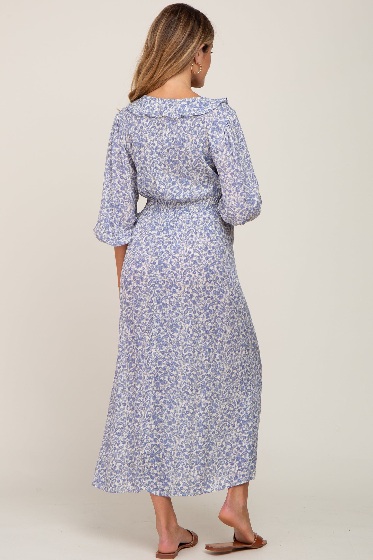 woman wearing a long sleeve light blue floral maternity dress, view from the back, with a flowing maxi skirt