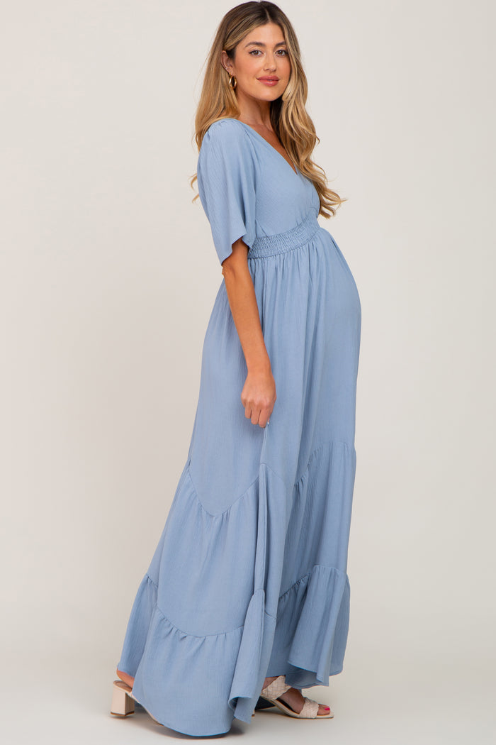 woman wearing a light blue maternity maxi dress with short sleeves and a tiered skirt, showing her baby bump